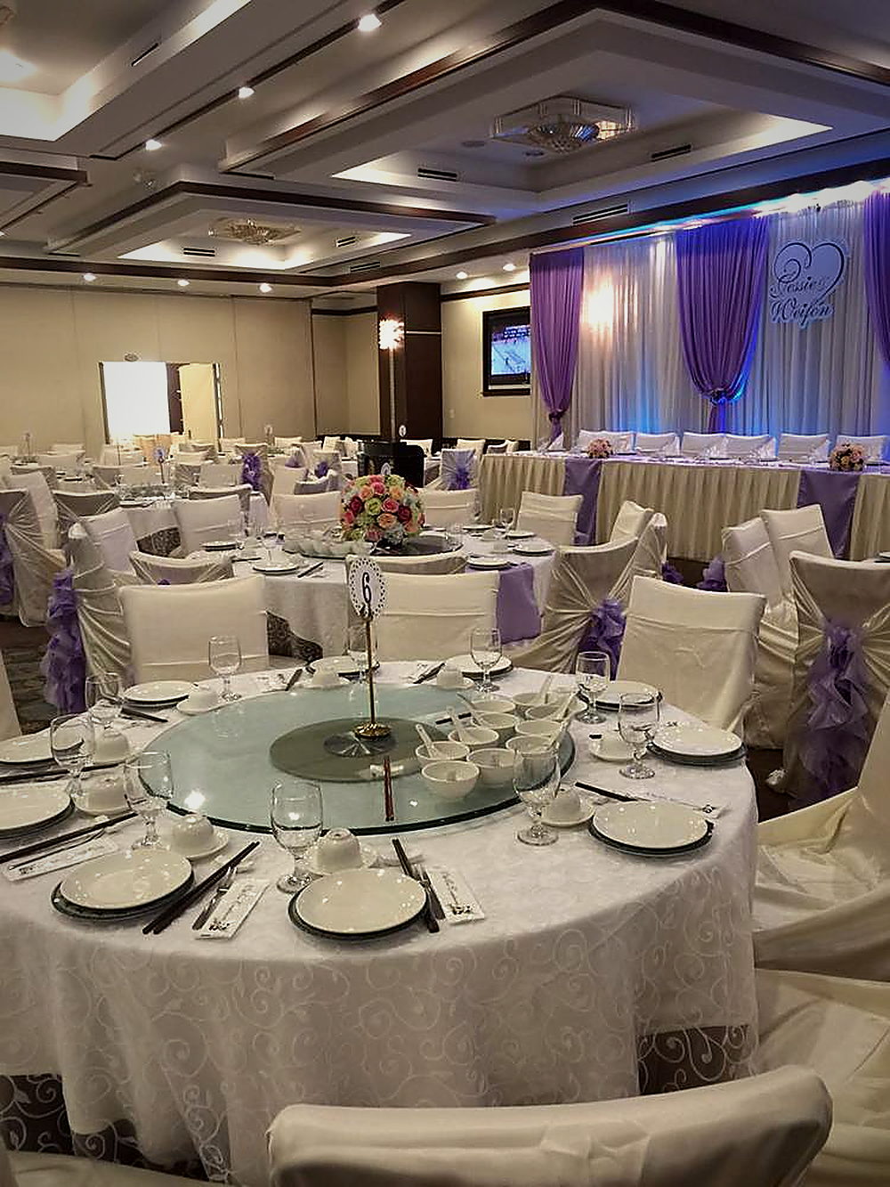 The banquet hall dressed for a wedding — round tables, chair sashes and the head table under lilac drapes